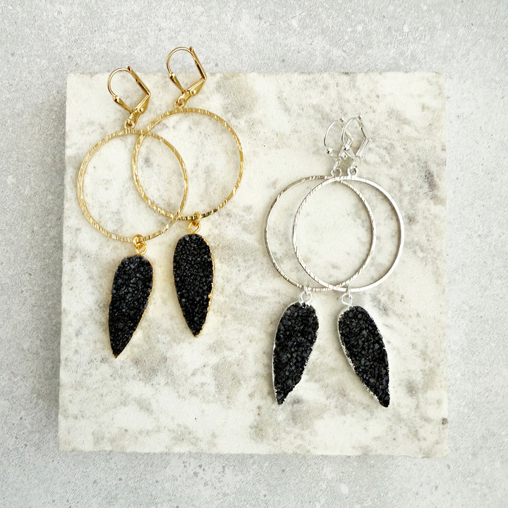 Pair of hoop earrings with black druzy charms on a marble surface