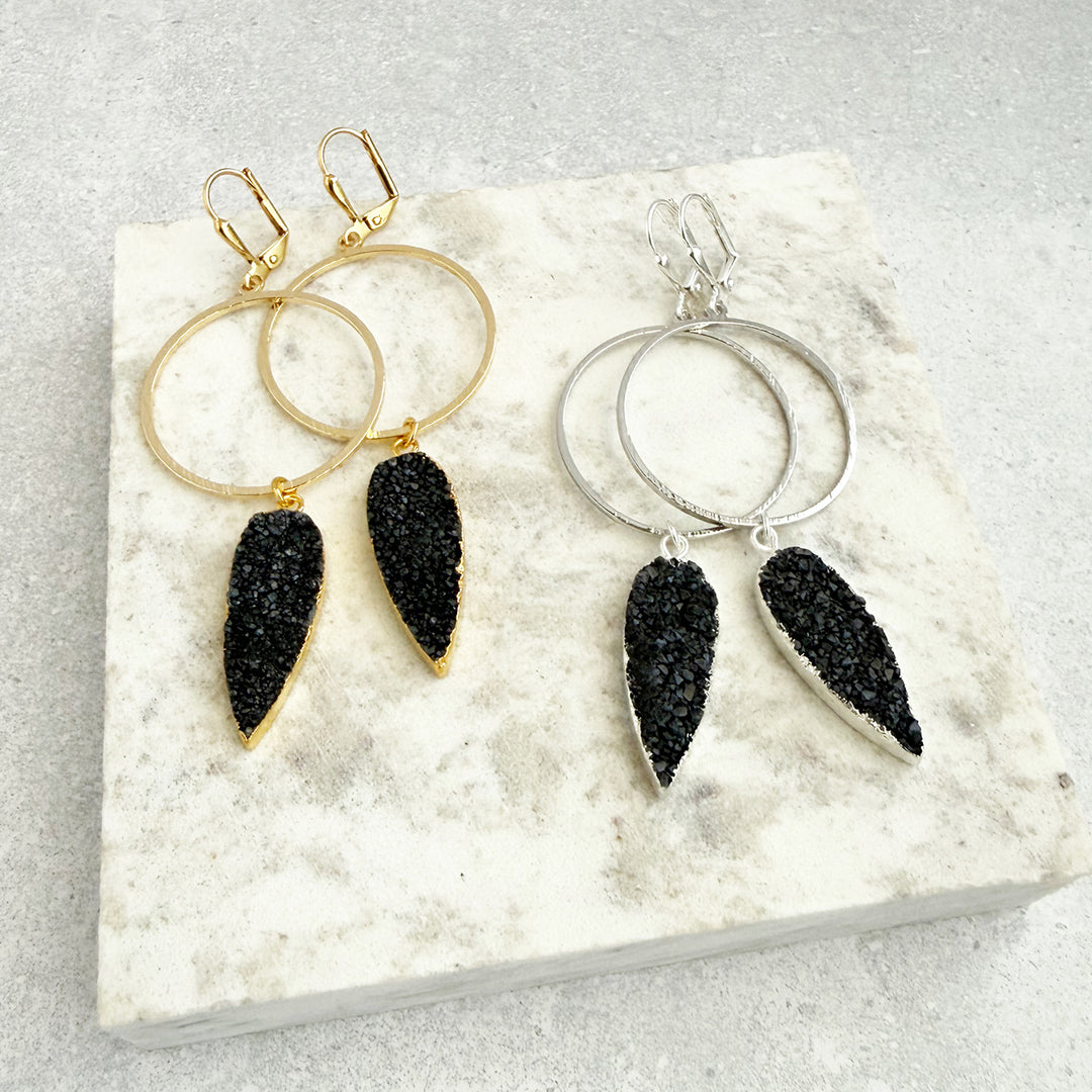 Pair of hoop earrings with black teardrop-shaped charms on a textured white surface.
