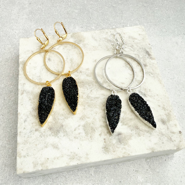 Pair of hoop earrings with black teardrop-shaped charms on a textured white surface.