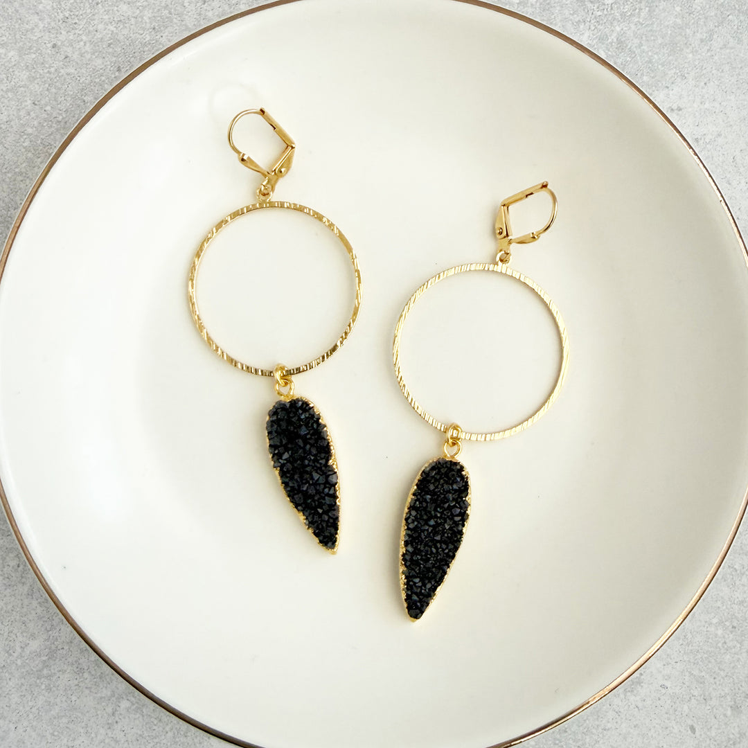Gold hoop earrings with black dangling stones on a white plate.