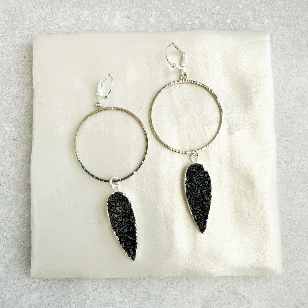 Silver hoop earrings with black druzy stones on a white cushion