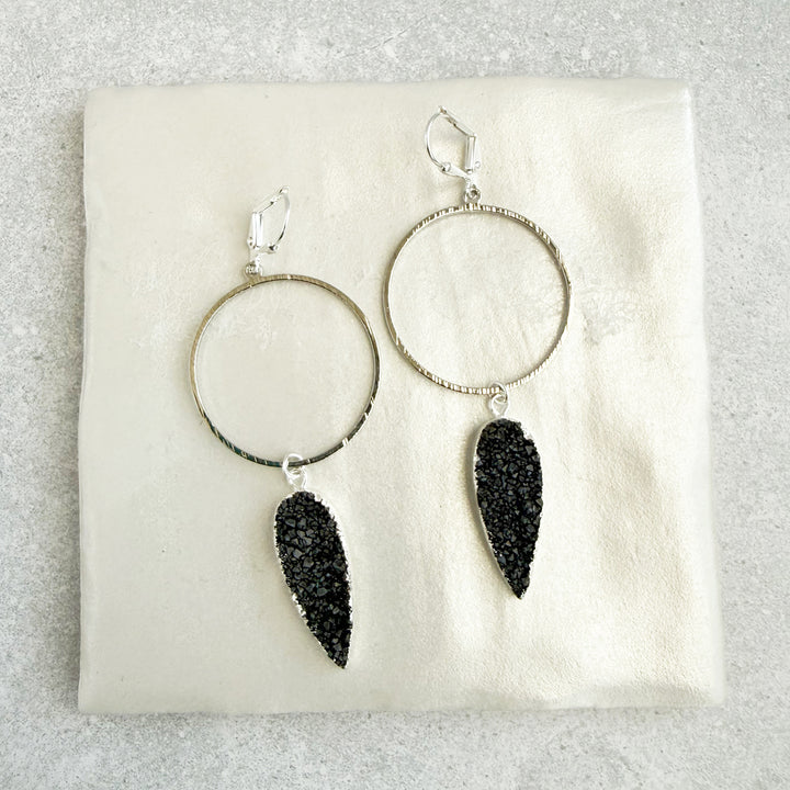 Silver hoop earrings with black druzy stones on a white cushion
