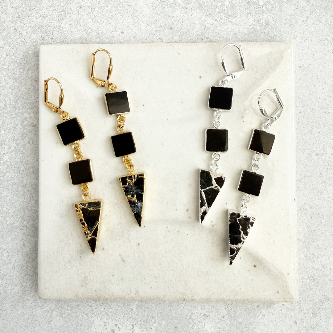 Two pairs of earrings on a marble surface, one gold and black, the other silver and black.