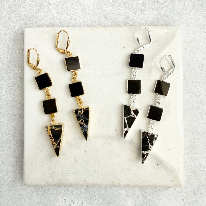 Two pairs of earrings on a marble surface, one gold and black, the other silver and black.