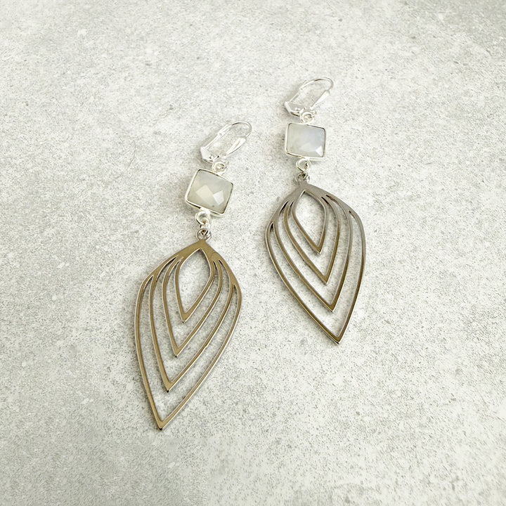 Pair of silver earrings with leaf-like designs on a textured gray background