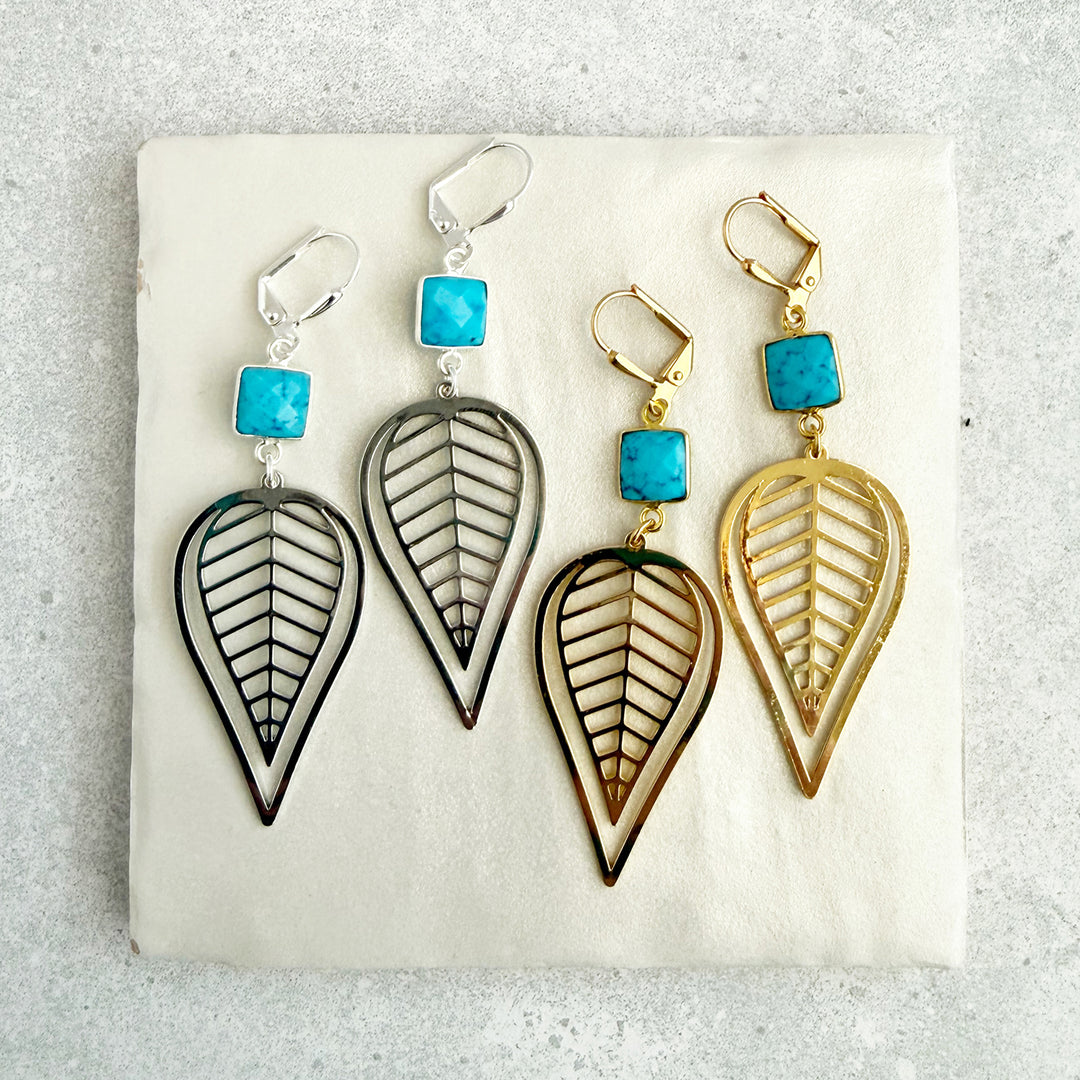Pair of earrings with leaf-shaped designs and turquoise stones on a light background