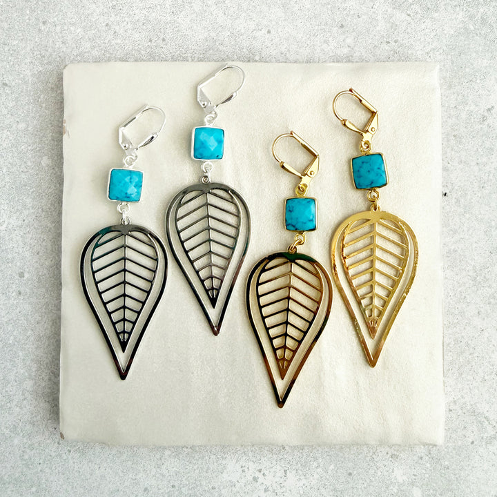 Pair of earrings with leaf-shaped designs and turquoise stones on a light background