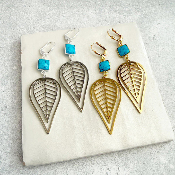 Pair of leaf-shaped earrings with turquoise stones on a white stone surface