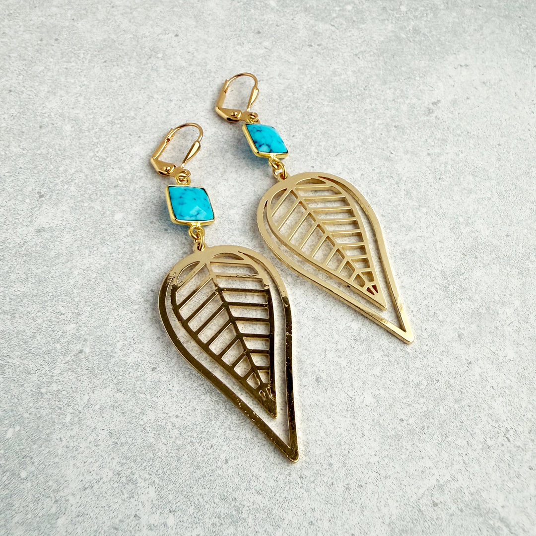 Gold leaf-shaped earrings with turquoise stones on a light gray background