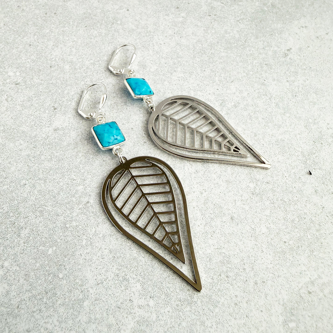 Pair of leaf-shaped earrings with turquoise stones on a textured gray surface
